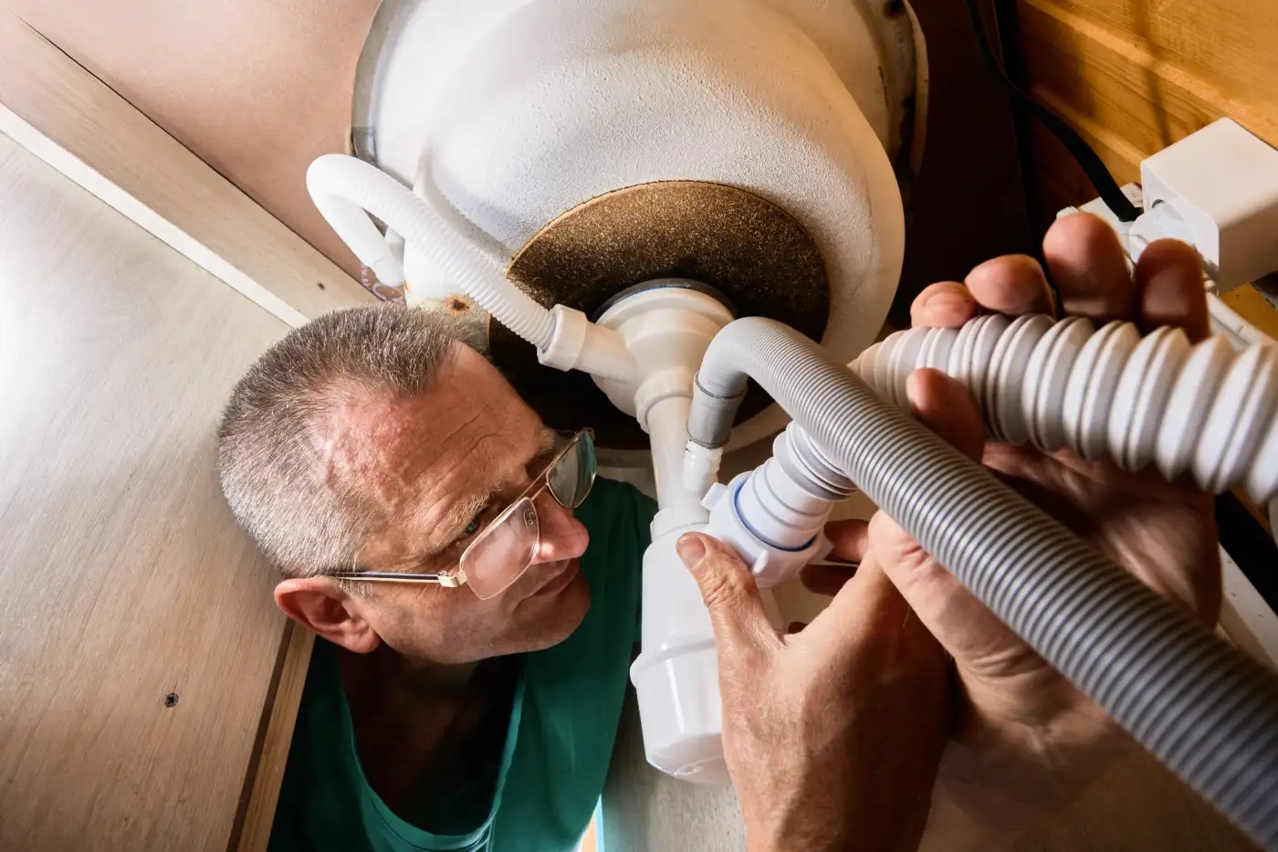 A plumber working on the U-bend trap under a sink
