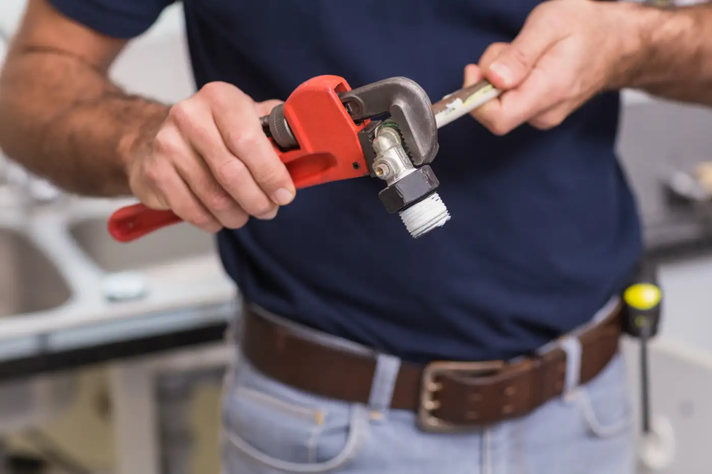 A plumber tightening a pipe fitting with a wrench