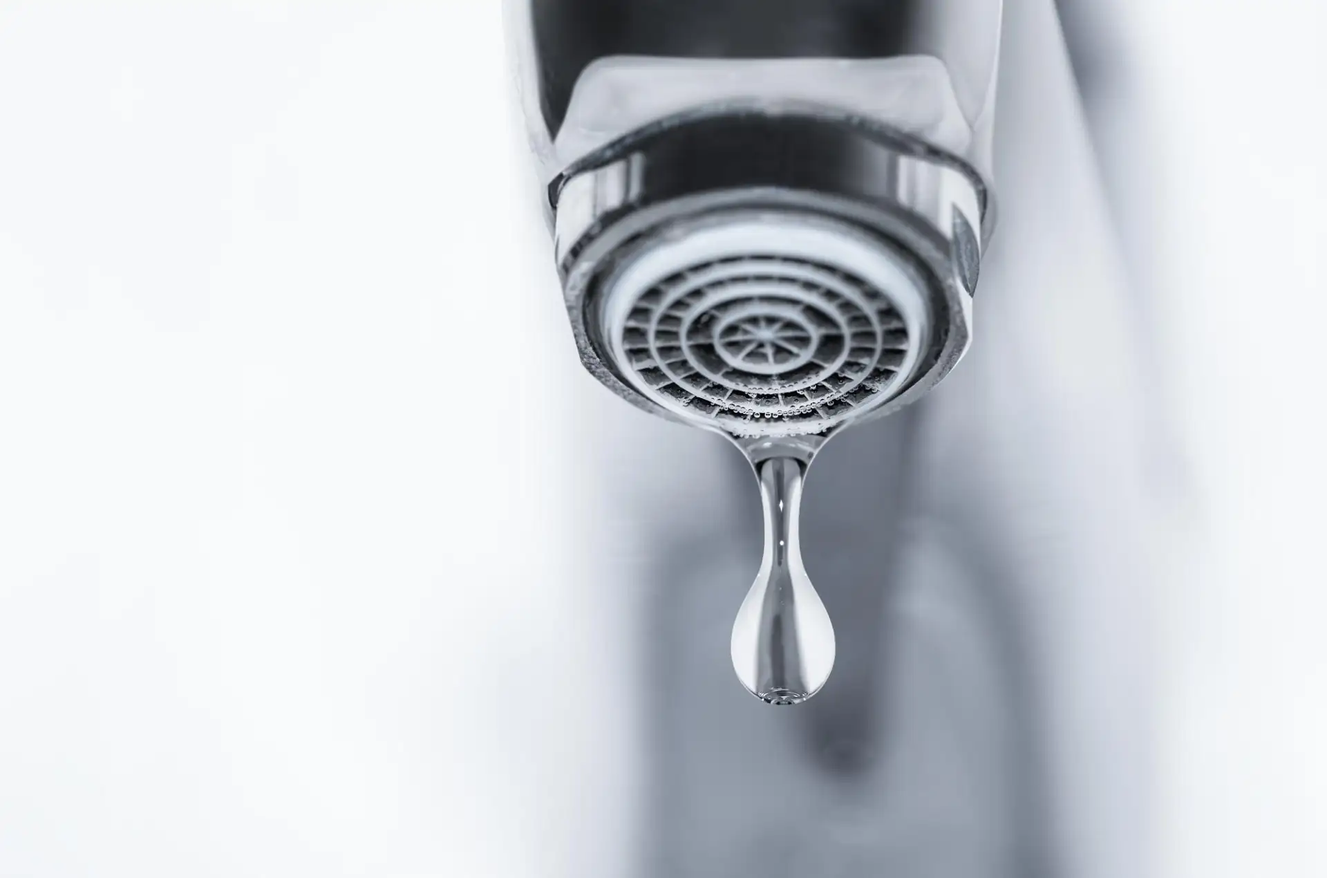 A hand steadying a dripping mixer tap with a spanner at a kitchen sink