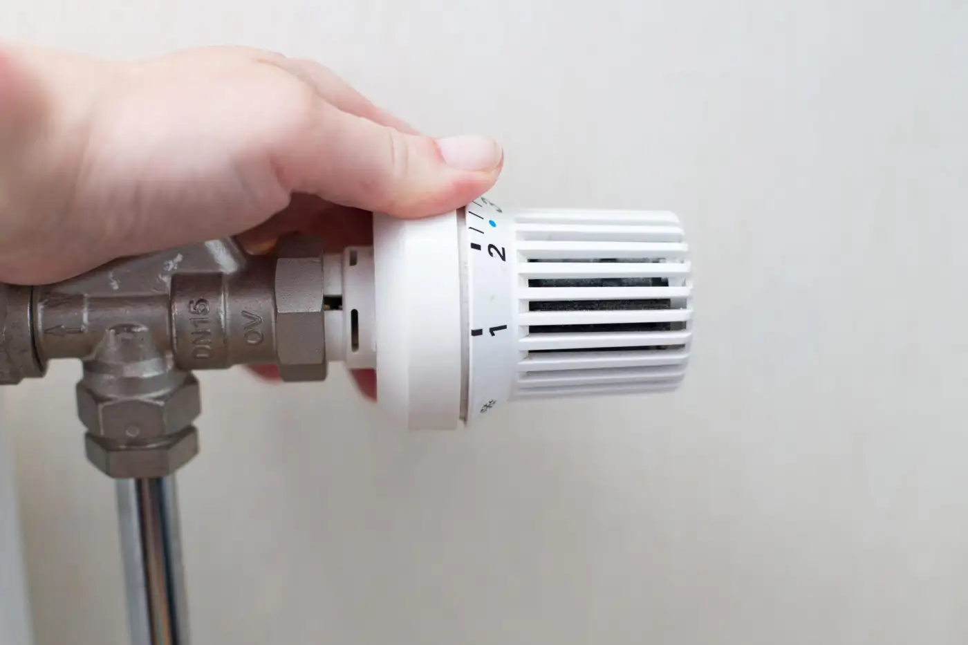 A hand turning the thermostatic valve on a domestic radiator