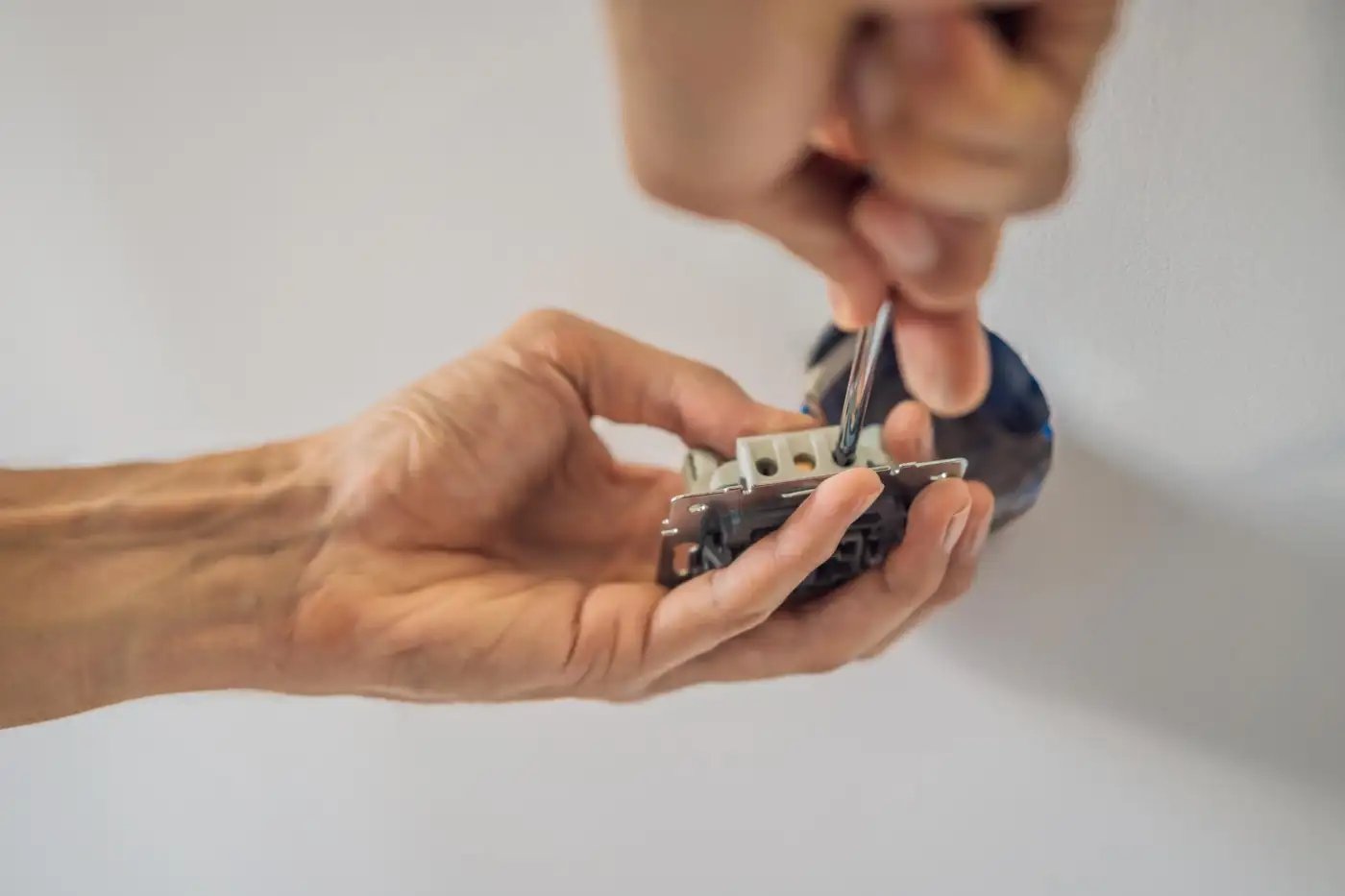An electrician's hands wiring a socket outlet