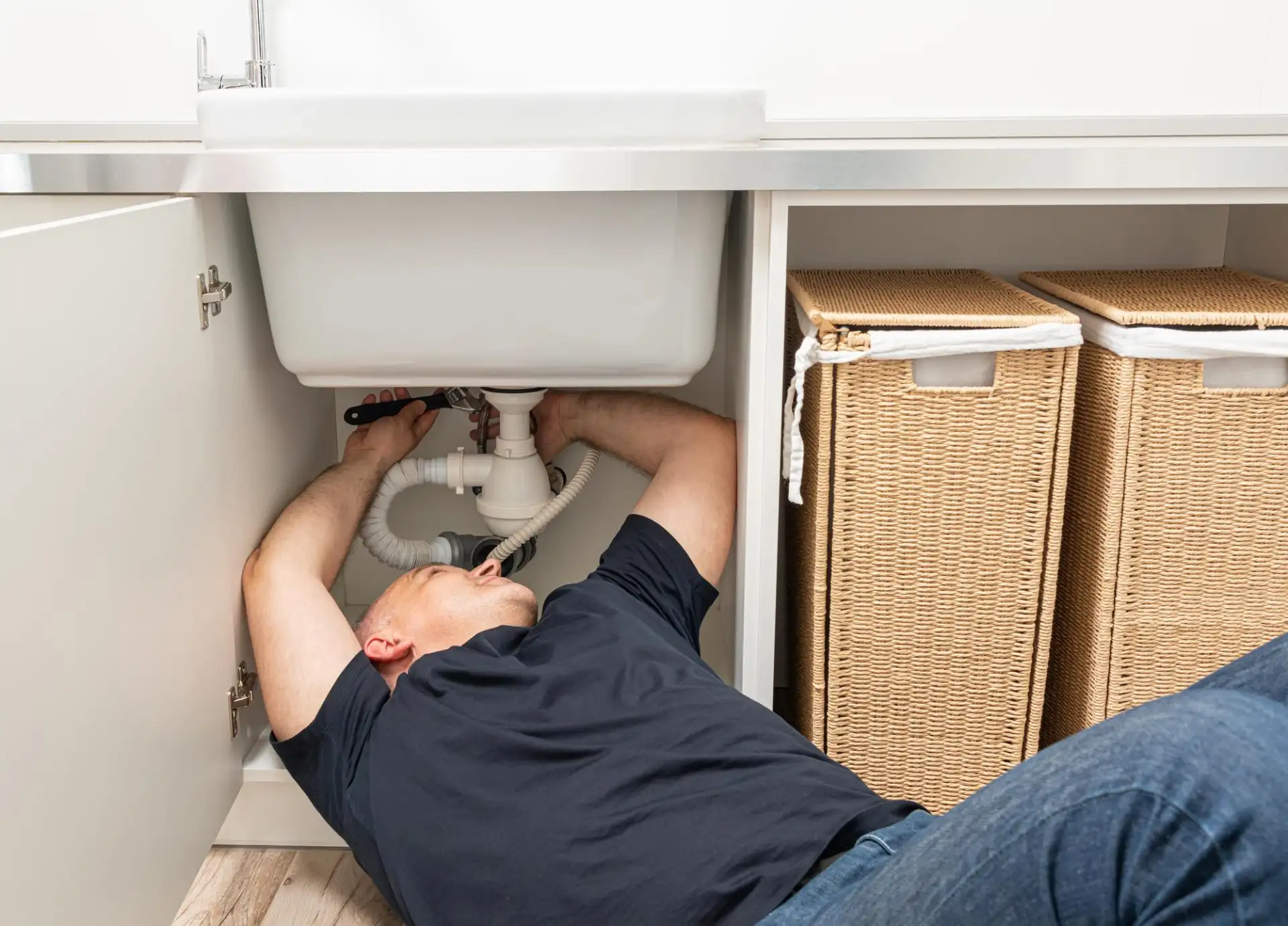 A plumber working on pipework under a kitchen sink with tools laid out