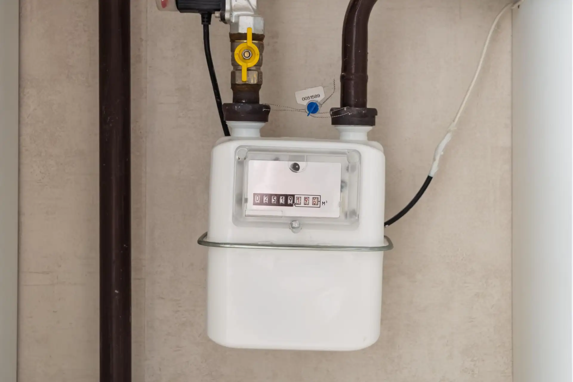 A domestic gas meter on a wall with its pipework and shut-off valve
