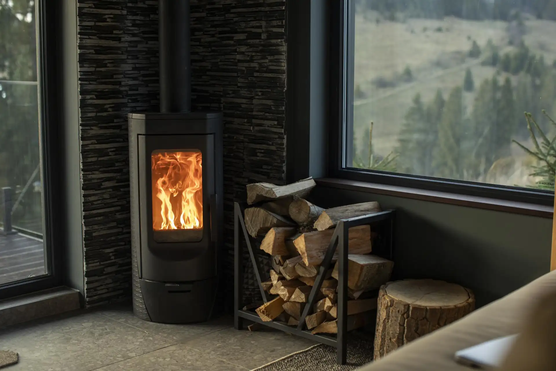 A wood-burning stove alight in a living room with logs stacked beside it